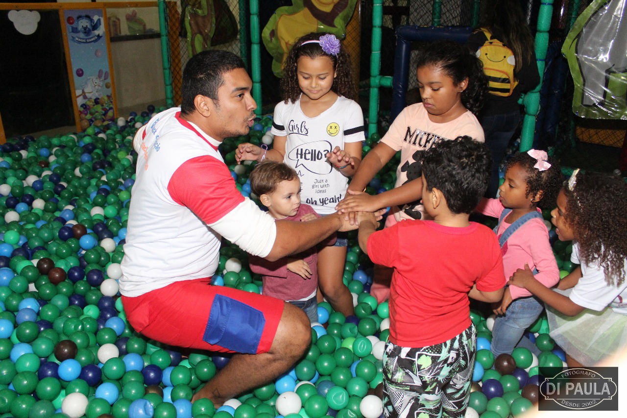 Crianças e um dos recreadores dentro da piscina de bolinhas coloridas formando um time para